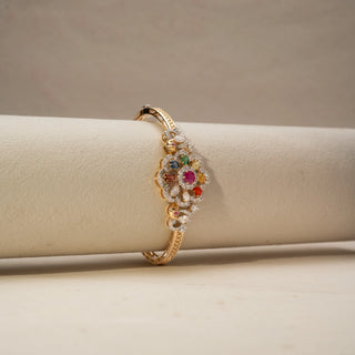 Side view of a multicolour gemstone and diamond bracelet in 14 KT Yellow Gold, featuring a floral cluster of vibrant gemstones framed by pavé-set diamonds, displayed against a soft beige backdrop.