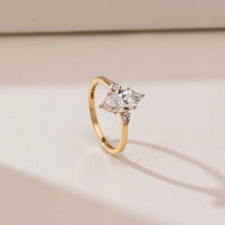 Angled view of yellow gold diamond ring featuring a marquise-cut lab-grown centre stone with pear-shaped side accents, highlighted against a soft neutral studio background.