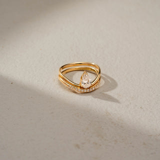 Top view of a pear solitaire ring in 14 KT Yellow Gold, featuring a bezel-set pear-shaped lab-grown diamond paired with a pavé-set curved band in a modern stacked design, displayed against a beige backdrop.