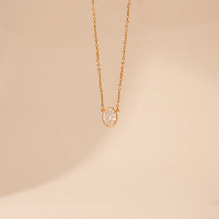 Front view of a 14KT yellow gold necklace featuring an oval-cut solitaire diamond pendant, set against a beige background.