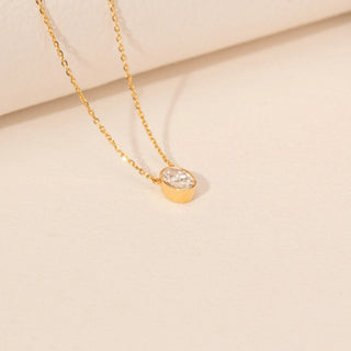 Angled view of a 14KT yellow gold necklace featuring an oval-cut solitaire diamond pendant, set against a beige background.