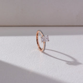 Side view of Radiant Solitaire Diamond Ring in 14KT Rose Gold, featuring a centred radiant-cut lab grown diamond with a pavé-set band. Set on a beige backdrop, the design highlights depth and brilliance.

