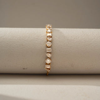 Front view of a gold bracelet featuring alternating round, pear, and emerald-cut gemstones in a linked design, displayed on a neutral cylindrical stand with elegant sparkle.