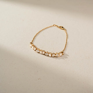 Top view of a delicate gold bracelet featuring alternating round, pear, and emerald-cut gemstones along a fine chain, elegantly displayed on a soft neutral background.