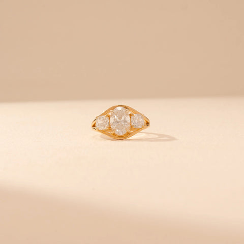 Front view of a 14KT yellow gold ring featuring oval and cushion-cut diamonds, set against a beige background.
