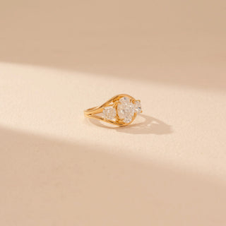 Side view of a 14KT yellow gold ring featuring oval and cushion-cut diamonds, set against a beige background.