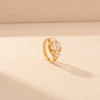 Angled view of a 14KT yellow gold ring featuring oval and cushion-cut diamonds, set against a beige background.