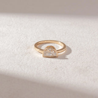 Top view of half-moon diamond ring in yellow gold with a slim band and bezel setting, set on a soft neutral surface, highlighting smooth curves and clean, radiant sparkle.
