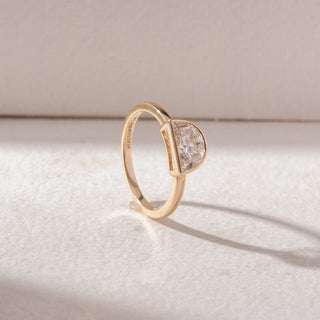 Angled view of half-moon diamond ring in yellow gold with a slim band and bezel setting, set on a soft neutral background, highlighting curved form and refined, radiant sparkle.
