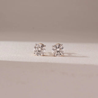 Front view of diamond stud earrings in 14KT yellow gold, featuring round brilliant diamonds in classic prong settings, displayed on a beige surface highlighting timeless sparkle and elegance.
