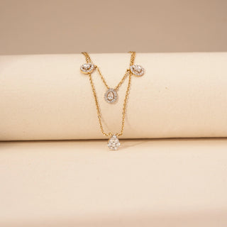 Front view of a pear-shaped lab-grown diamond layered necklace in 14KT Yellow Gold, featuring halo-set pear and oval motifs. Captured against a beige backdrop, the elegant layered design radiates timeless sparkle.