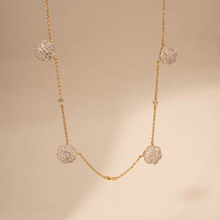 Front view of a floral lab-grown diamond station necklace in 18KT Yellow Gold, featuring round diamond cluster motifs spaced along a delicate chain. Captured against a beige backdrop, the elegant design radiates timeless sparkle.