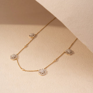 Angled view of a floral lab-grown diamond station necklace in 18KT Yellow Gold, featuring round diamond cluster motifs along a delicate chain. Captured against a beige backdrop, the graceful design radiates timeless sparkle.