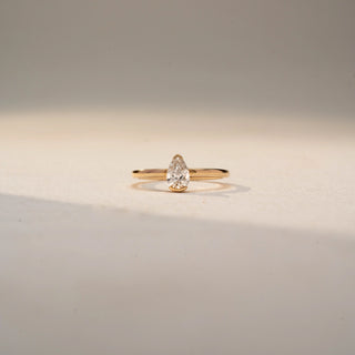 Front view of a pear solitaire ring in 14 KT Yellow Gold, featuring a pear-shaped lab-grown diamond in a classic three-prong setting, displayed against a beige backdrop.
