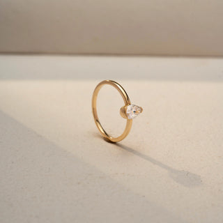 Angled view of a pear solitaire ring in 14 KT Yellow Gold, featuring a pear-shaped lab-grown diamond in a classic three-prong setting, displayed against a beige backdrop.

