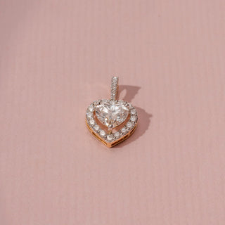 Angled view of a 14KT white gold pendant featuring heart and round-cut diamonds, set against a pink background.