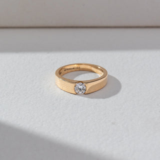 Top view of Bezel Set Diamond Band Ring in 14KT Yellow Gold, featuring a single round lab grown diamond set in a smooth band. Set on a beige backdrop, the design highlights symmetry and minimal elegance.
