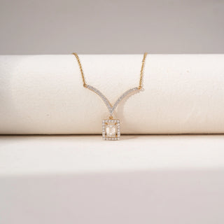 Close up view of an emerald-cut lab-grown diamond pendant necklace in 14KT Dual Gold, featuring a halo-set emerald-cut centre stone suspended from a curved diamond bar. Captured against a beige backdrop, the elegant design radiates brilliance.