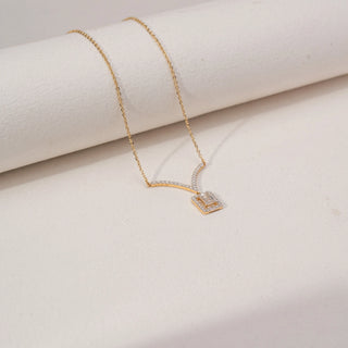 Angled view of an emerald-cut lab-grown diamond pendant necklace in 14KT Dual Gold, featuring a halo-set emerald-cut centre stone suspended from a curved diamond bar. Captured against a beige backdrop, the elegant design radiates brilliance.