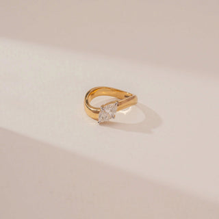 Close-up view of a marquise diamond ring in 14KT Yellow Gold, featuring a wide polished band and four-prong setting against a beige backdrop.