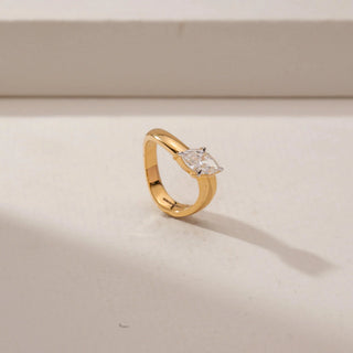 Angled view of a marquise diamond ring in 14KT Yellow Gold, featuring a wide polished band and four-prong setting against a beige backdrop.