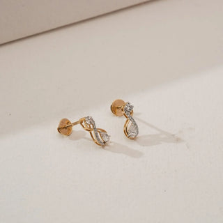 Angled side view of infinity loop diamond earrings with round and pear-shaped lab-grown diamonds set in yellow gold, showcasing the curved drop design and delicate pavé detailing.