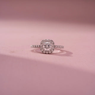 Front view of a cushion halo engagement ring in White Gold, featuring a cushion-cut lab-grown diamond encircled by a sparkling halo and set on a pavé diamond band, displayed against a soft pink backdrop.