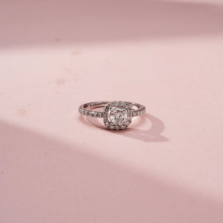 Top view of a cushion halo engagement ring in White Gold, featuring a cushion-cut lab-grown diamond encircled by a sparkling halo and set on a pavé diamond band, displayed against a soft pink backdrop.
