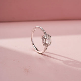 Angled view of a cushion halo engagement ring in White Gold, featuring a cushion-cut lab-grown diamond encircled by a sparkling halo and set on a pavé diamond band, displayed against a soft pink backdrop.
