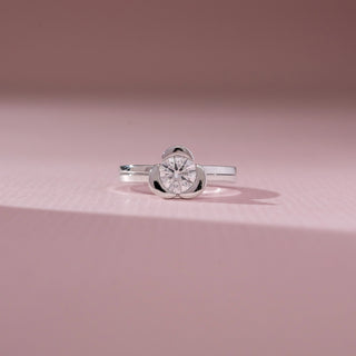 Front view of solitaire diamond ring in white gold, featuring a round lab-grown diamond held in a smooth bezel-style setting. Captured against a soft pink background with gentle shadows.