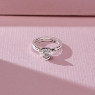 Top angled view of solitaire diamond ring in white gold, featuring a round lab-grown diamond in a smooth bezel-style setting. Set against a soft pink textured background with gentle shadows.