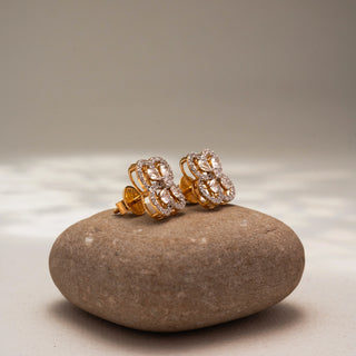 Side view of floral diamond stud earrings in 14 KT Yellow Gold, featuring four petal-inspired pavé diamond loops with pear-shaped diamond accents, displayed on a textured stone surface.