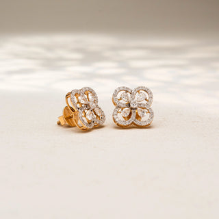 Angled view of floral diamond stud earrings in 14 KT Yellow Gold, featuring four petal-inspired pavé diamond loops with pear-shaped diamond accents, displayed on a textured stone surface.