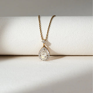 Top view of Teardrop Halo Diamond Pendant Necklace in 14KT Yellow Gold, featuring a pear-shaped lab grown diamond encircled by a halo and a round accent above. Set on a beige backdrop, the design highlights radiant sparkle and elegance.
