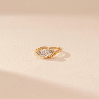 Close-up view of a 14KT yellow gold ring featuring a marquise-cut diamond in a bezel setting, set against a beige background.