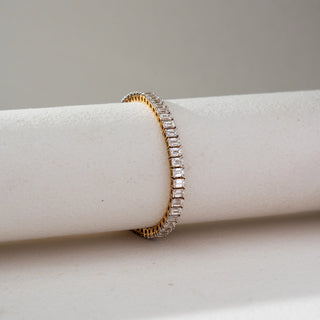 Side view of Emerald Cut Diamond Tennis Bracelet in 14KT Dual Gold, featuring a continuous row of emerald-cut lab grown diamonds in a prong setting. Placed on a beige backdrop, the design highlights sleek brilliance and elegance.
