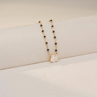 Close up view of a solitaire diamond mangalsutra in Dual gold, featuring a round-cut diamond pendant on a delicate black bead chain, styled against a soft beige backdrop.