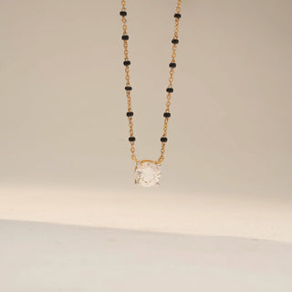 Front view of a solitaire diamond mangalsutra in Dual gold, featuring a round-cut diamond pendant on a black bead chain, suspended against a soft beige backdrop.