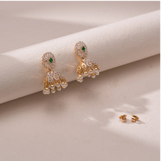 Angled view of the Royal Emerald Pearl Jhumka Earrings in 14KT yellow gold, featuring pear-shaped diamonds, emerald-toned center stones, and pearl danglers. The design reflects regal elegance and grandeur.
