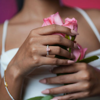 Close-up of Reia Rose Glow Radiant Diamond Ring worn while holding pink roses, highlighting the radiant-cut pink diamond on a white gold band with pave diamonds, evoking grace and emotion.