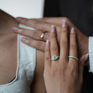 Close-up of Reia Verdant Halo Radiant Diamond Ring worn by a woman's hand beside a partner's, symbolising love and individuality, featuring a radiant green diamond and halo setting in white gold.