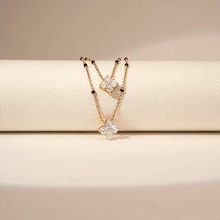 Close up view of a 14KT Yellow Gold diamond necklace with two layered chains, black bead accents and two clustered diamond pendants.