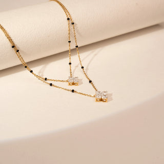 Top view of a 14KT Yellow Gold diamond necklace with two layered chains, black bead accents and two clustered diamond pendants.