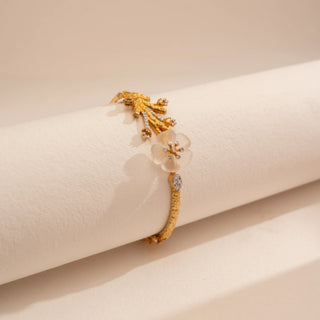 Side view of Reia’s 14 KT Yellow Gold Floral Carved Shell Diamond Bracelet. Captured on a cream backdrop, it highlights the textured gold branch and the ethereal glow of the carved shell blossom.