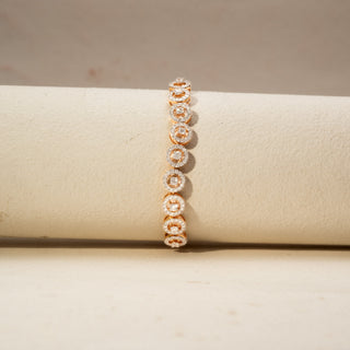 Front view of a diamond halo station bracelet in 14 KT Rose Gold, featuring cushion-shaped lab-grown diamonds framed by sparkling halo settings, displayed on a beige surface.