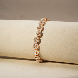 Close up view of a diamond halo station bracelet in 14 KT Rose Gold, featuring cushion-shaped lab-grown diamonds framed by sparkling halo settings with elevated profiles, displayed on a beige surface.