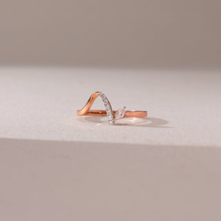 Front view of a diamond ring in 9KT rose gold, featuring a curved pavé band with a marquise diamond accent, set on a beige surface highlighting modern elegance and delicate sparkle.

