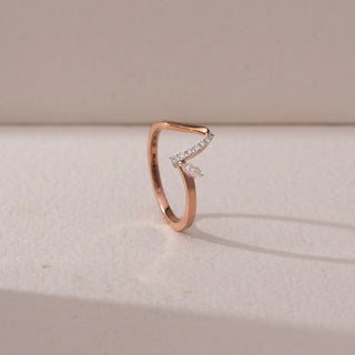 Angled view of a diamond ring in 9KT rose gold, featuring a curved pavé band with a marquise diamond accent, displayed on a beige surface, highlighting modern elegance and refined sparkle.
