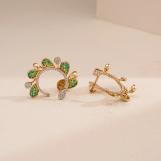 Angled view of Reia’s 14 KT Yellow Gold Emerald Enamel Winged Diamond Earrings. It highlights the feather-like emerald enamel patterns and curved round brilliant diamonds against a cream backdrop.