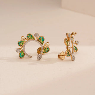 Angled front view of Reia’s 14 KT Yellow Gold Emerald Enamel Winged Diamond Earrings. It highlights the intricate green enamel wing patterns and curved round diamonds against a clean, cream backdrop.